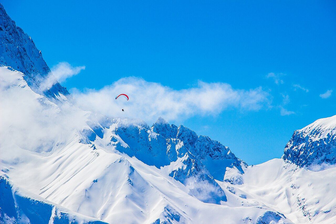 Parapente biplace rouge au-dessus des sommets des Écrins, vu depuis Les 2 Alpes