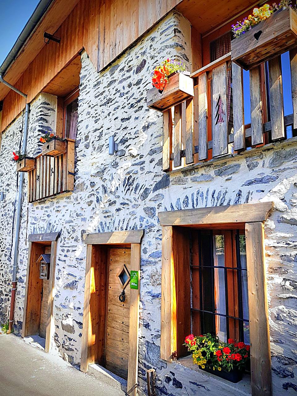 La façade en pierre du Cosy Lodge et ses balcons fleuris, au centre du Bourg-d'Oisans