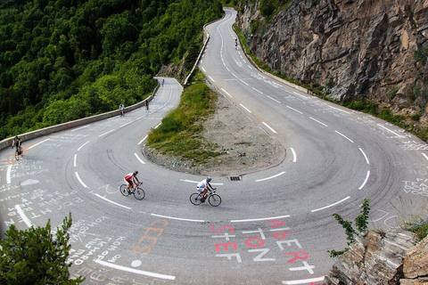 Cyclistes dans une épingle de l'Alpe d'Huez, sur un bitume couvert de noms peints par les supporters