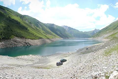 Panorama du lac de Grand'Maison à niveau bas, avec la route des cols à droite, au pied des alpages