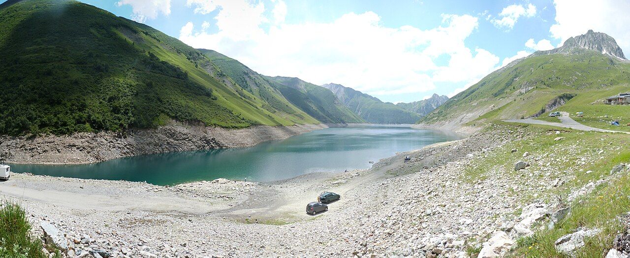 Panorama du lac de Grand'Maison à niveau bas, avec la route des cols à droite, au pied des alpages