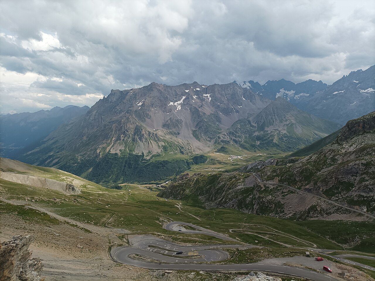 Vue du sommet du Galibier sur les lacets de la route et le col du Lautaret, sous un ciel chargé