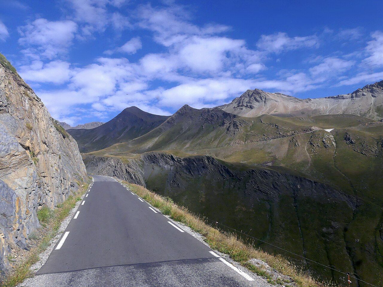 La route étroite du Galibier longe une paroi rocheuse au-dessus des alpages, côté Hautes-Alpes