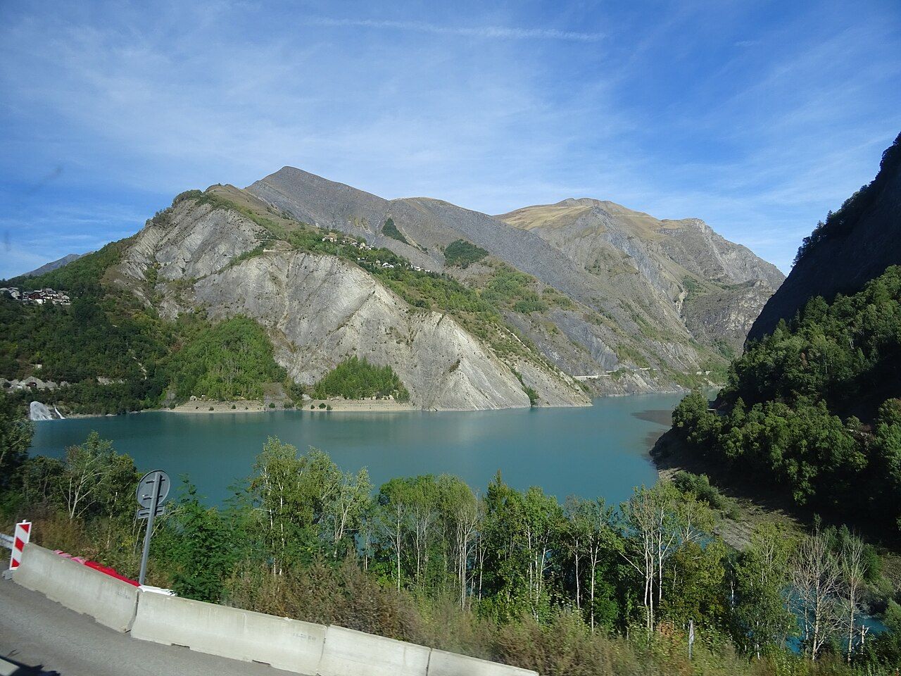 Le lac du Chambon, eau turquoise et versants gris, vu depuis la D213 qui monte aux 2 Alpes