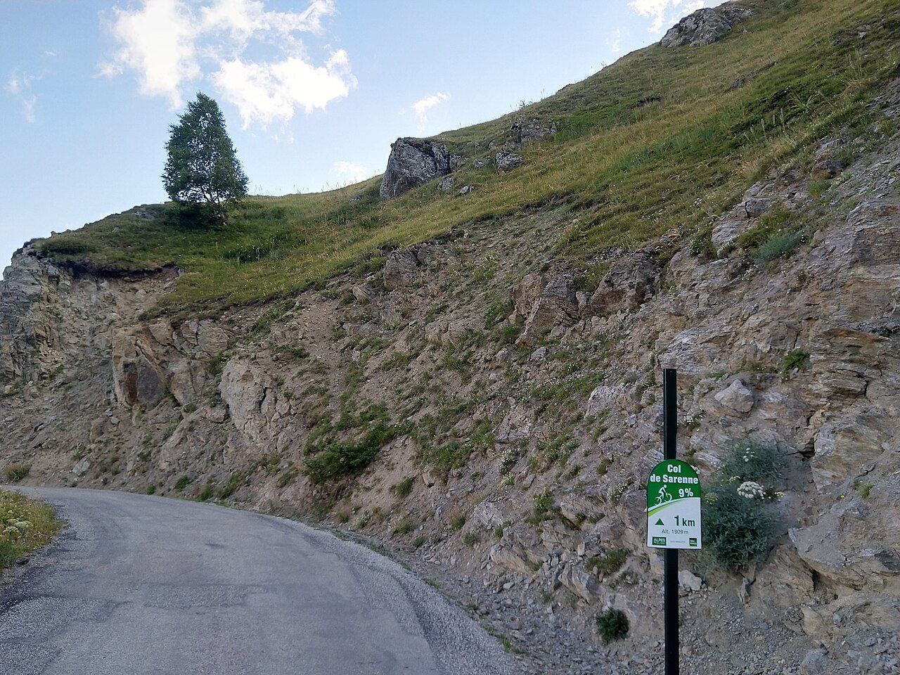 Panneau cycliste du col de Sarenne indiquant 1 km à 9 % à 1 909 m, au bord de la route étroite taillée dans la roche