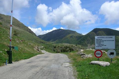 Route pastorale du col de Sarenne côté Alpe d'Huez, avec barrière, panneaux et alpages sous un ciel bleu