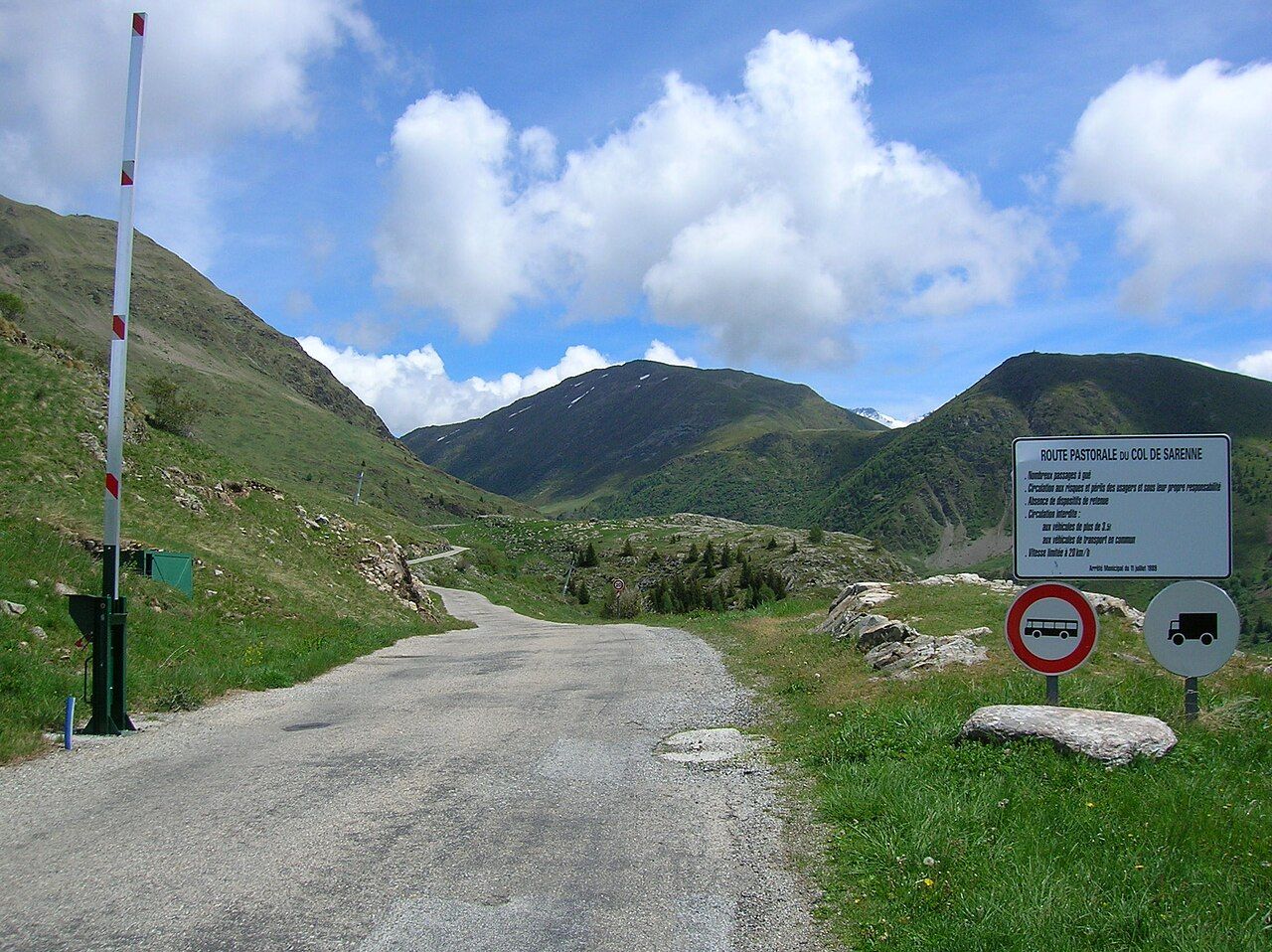 Route pastorale du col de Sarenne côté Alpe d'Huez, avec barrière, panneaux et alpages sous un ciel bleu