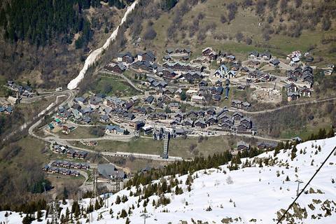 Vaujany vu d'en haut au printemps, ses chalets, la gare du téléphérique et la route du village, neige au premier plan